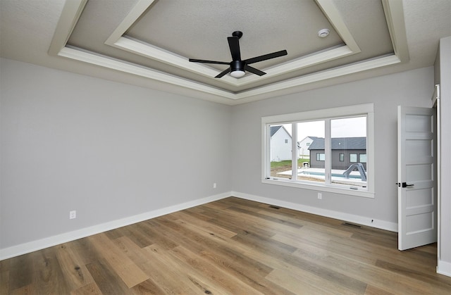 empty room with a tray ceiling, wood finished floors, baseboards, and ceiling fan