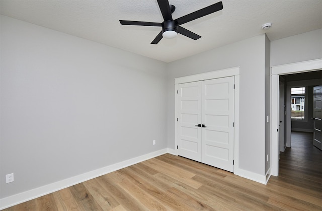 unfurnished bedroom featuring a ceiling fan, a textured ceiling, a closet, light wood-style floors, and baseboards