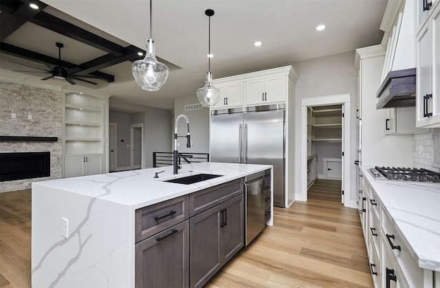 kitchen with a stone fireplace, a sink, stainless steel appliances, light wood-style flooring, and recessed lighting