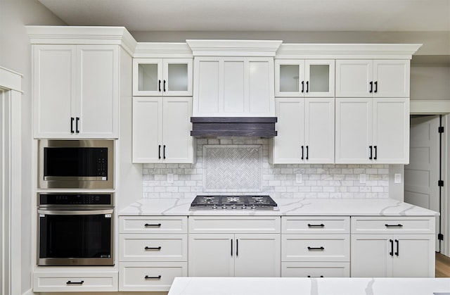 kitchen featuring white cabinets, backsplash, under cabinet range hood, and stainless steel appliances
