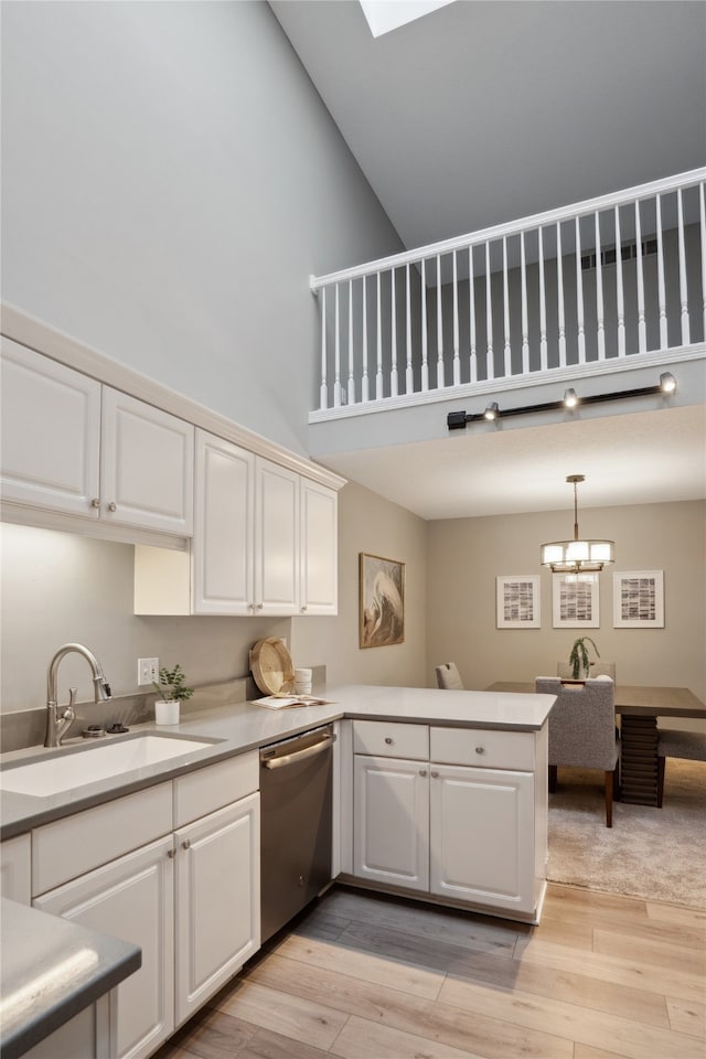 kitchen featuring stainless steel dishwasher, pendant lighting, light wood-type flooring, and high vaulted ceiling