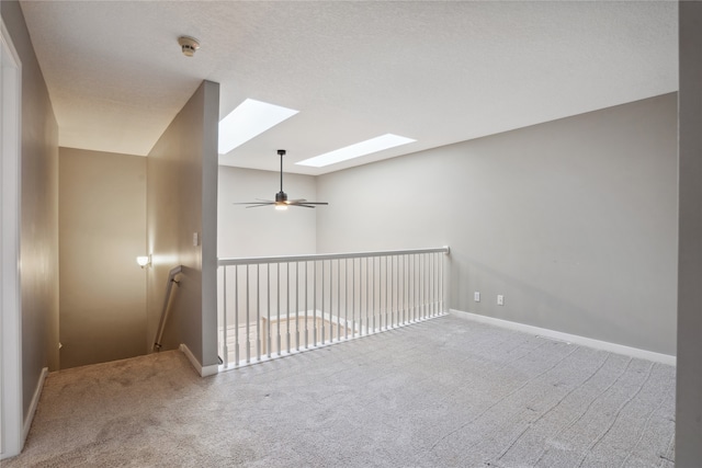 unfurnished room with carpet flooring, a skylight, ceiling fan, and a textured ceiling