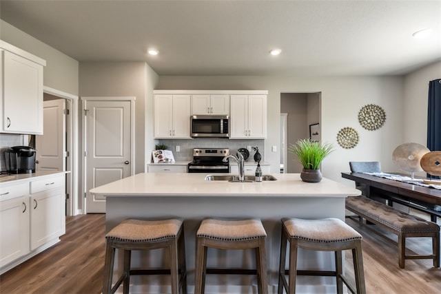 kitchen with stainless steel appliances, decorative backsplash, white cabinetry, a sink, and a kitchen bar