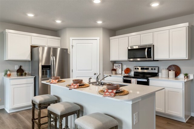 kitchen with a kitchen island with sink, white cabinets, sink, light wood-type flooring, and appliances with stainless steel finishes