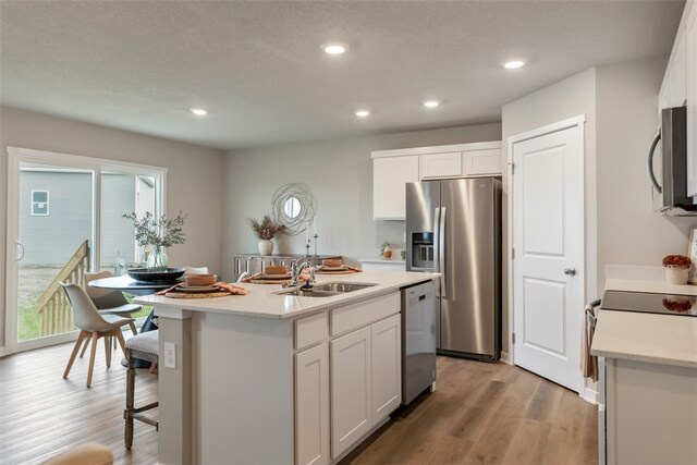 kitchen featuring sink, an island with sink, appliances with stainless steel finishes, light hardwood / wood-style floors, and white cabinetry