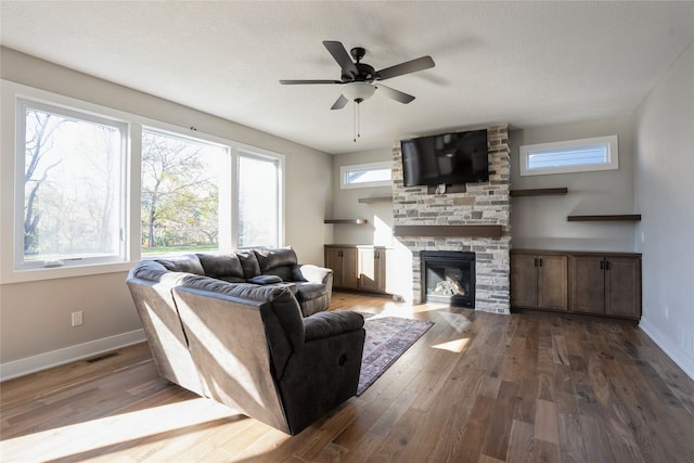 living room featuring dark hardwood / wood-style floors, ceiling fan, a stone fireplace, and a textured ceiling