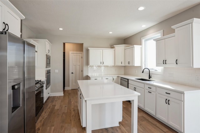 kitchen featuring appliances with stainless steel finishes, dark hardwood / wood-style flooring, sink, a center island, and white cabinetry