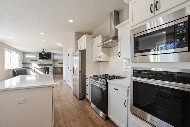 kitchen featuring wall chimney exhaust hood, stainless steel appliances, ceiling fan, dark hardwood / wood-style floors, and white cabinetry