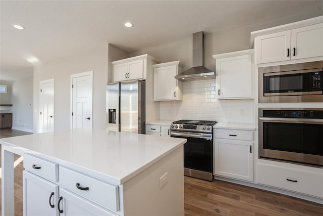 kitchen featuring dark wood-type flooring, white cabinets, wall chimney range hood, a kitchen island, and stainless steel appliances