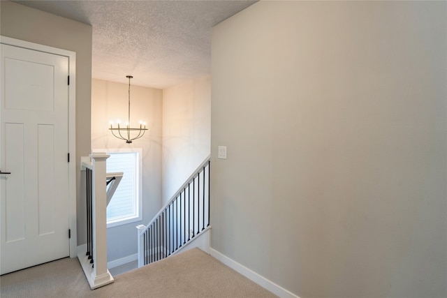 stairs with carpet, a notable chandelier, and a textured ceiling