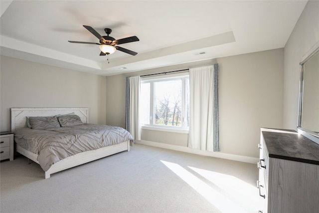 carpeted bedroom with a tray ceiling and ceiling fan