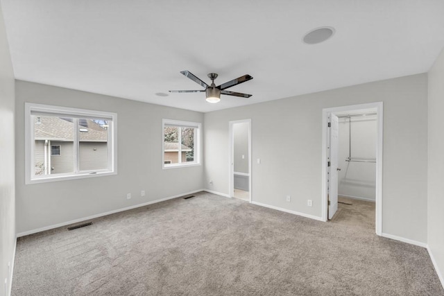 unfurnished bedroom with light carpet, a walk in closet, a closet, and ceiling fan