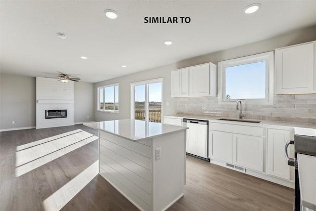 kitchen featuring sink, dishwasher, white cabinetry, a center island, and a large fireplace