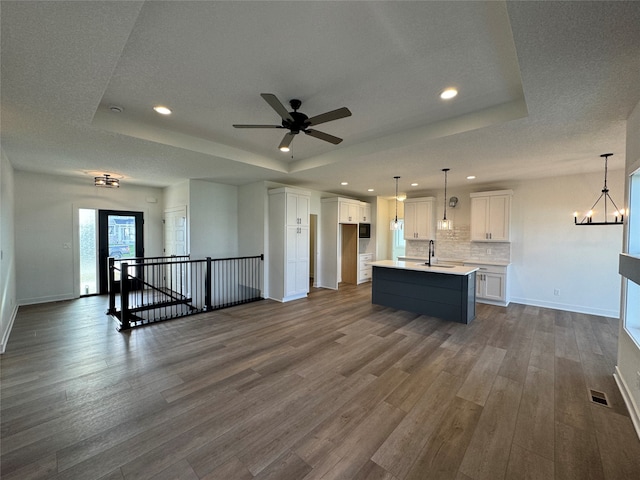 kitchen featuring white cabinets, a raised ceiling, wood-type flooring, and a kitchen island with sink