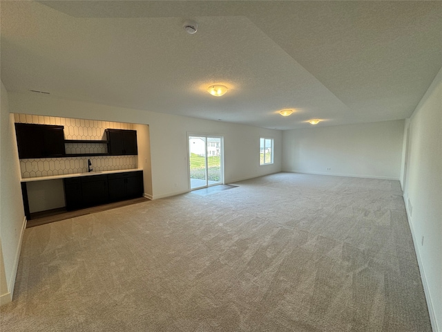 interior space with a textured ceiling, light colored carpet, and sink