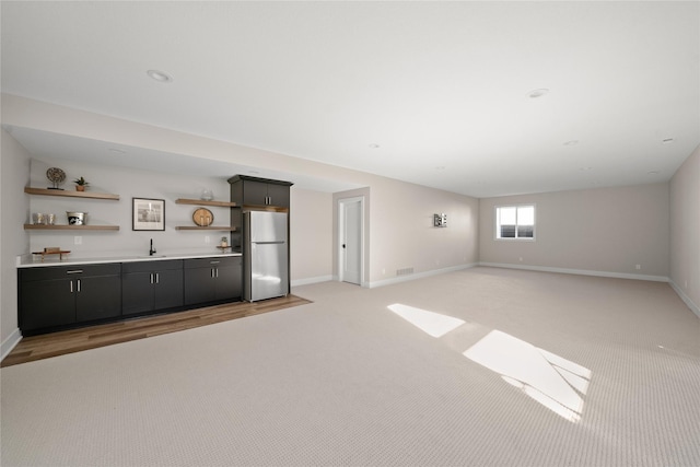 unfurnished living room featuring a sink, baseboards, wet bar, and light carpet