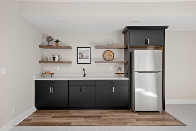 kitchen with open shelves, light countertops, light wood-style flooring, freestanding refrigerator, and a sink