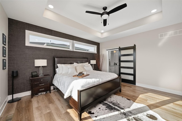 bedroom featuring a tray ceiling, a barn door, visible vents, and light wood finished floors