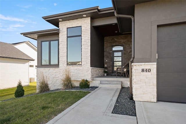 view of exterior entry featuring covered porch, stucco siding, a garage, stone siding, and a lawn