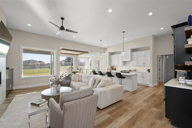 living area with baseboards, recessed lighting, a ceiling fan, and light wood-style floors