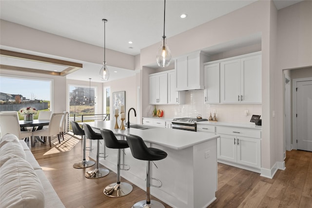 kitchen featuring a breakfast bar area, wood finished floors, high end stove, a sink, and tasteful backsplash