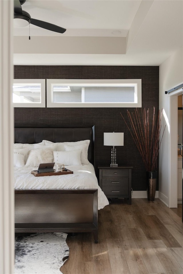 bedroom with a ceiling fan, a barn door, wood finished floors, and baseboards