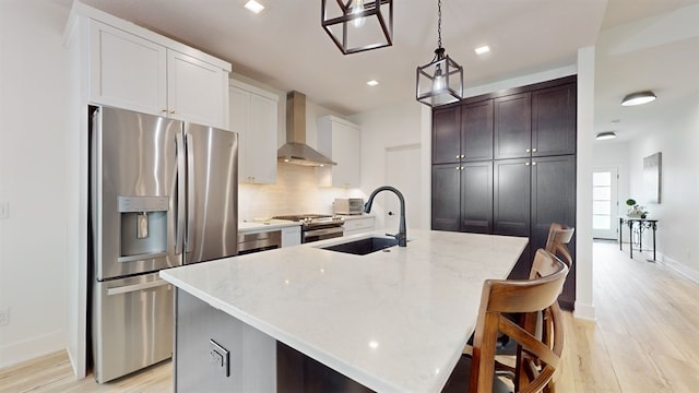 kitchen featuring appliances with stainless steel finishes, light hardwood / wood-style floors, a kitchen island with sink, and wall chimney exhaust hood