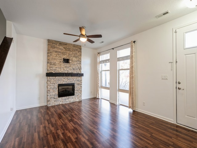 unfurnished living room with ceiling fan, a stone fireplace, and dark wood-type flooring