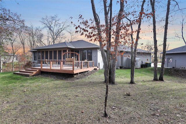 back house at dusk featuring a wooden deck, a lawn, and a sunroom