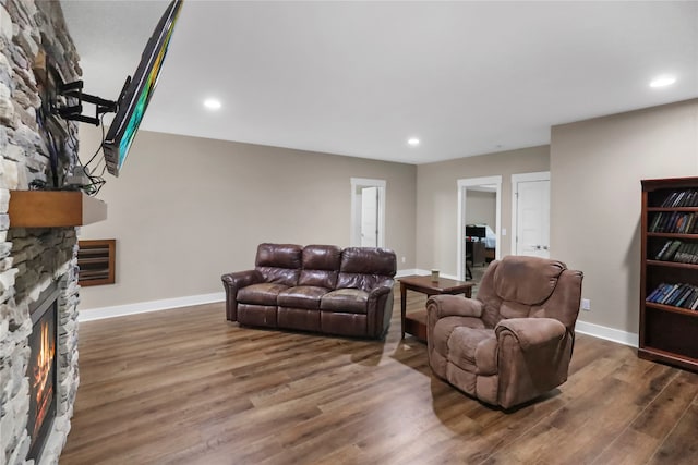 living room featuring a stone fireplace and dark hardwood / wood-style flooring