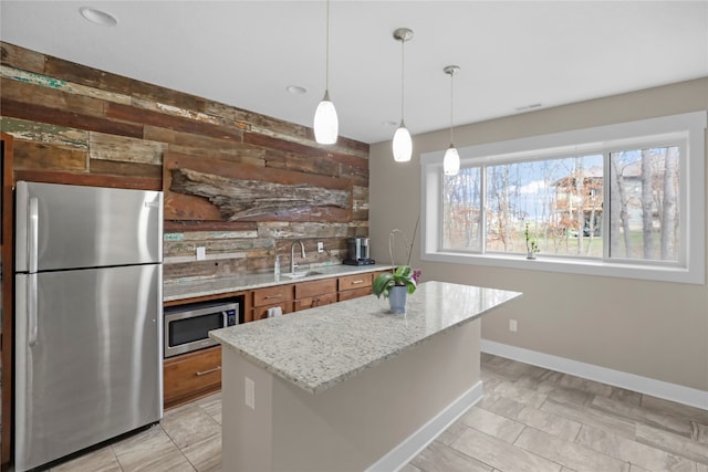 kitchen with sink, stainless steel appliances, light stone counters, decorative light fixtures, and a kitchen island