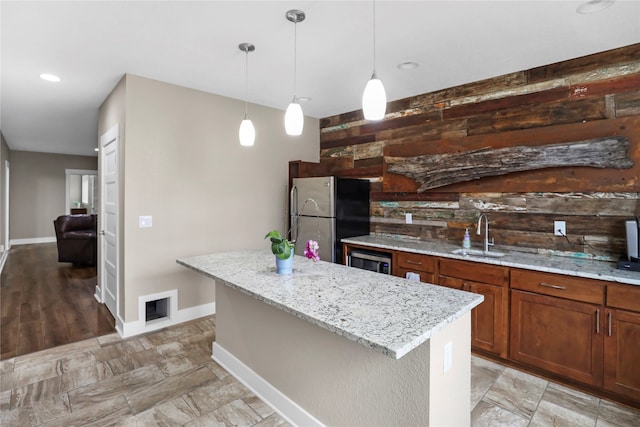 kitchen featuring a center island with sink, sink, hanging light fixtures, stainless steel fridge, and light stone counters