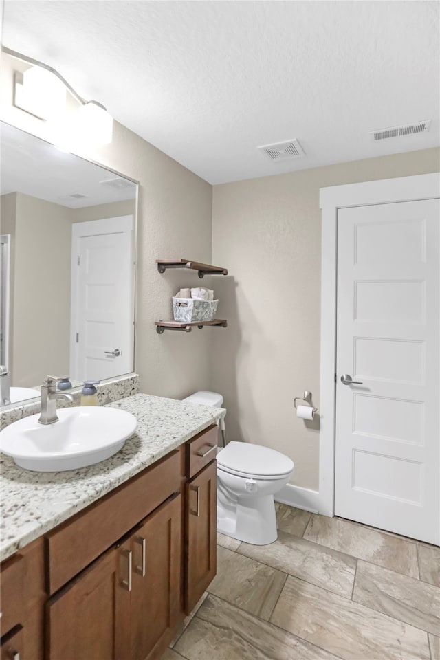 bathroom with a textured ceiling, vanity, and toilet