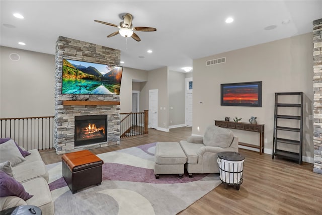 living room featuring hardwood / wood-style floors, a stone fireplace, and ceiling fan