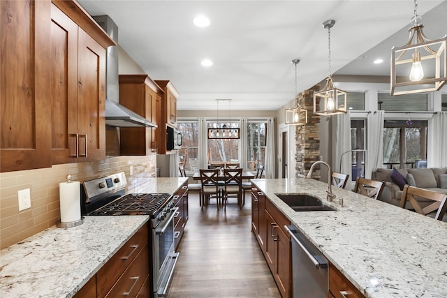 kitchen featuring pendant lighting, stainless steel appliances, wall chimney exhaust hood, and sink