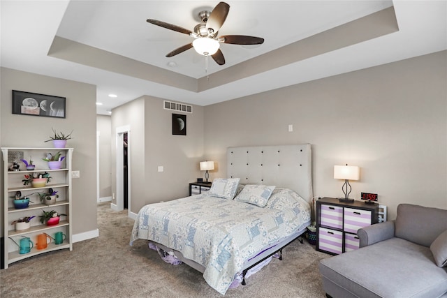 carpeted bedroom with a raised ceiling and ceiling fan