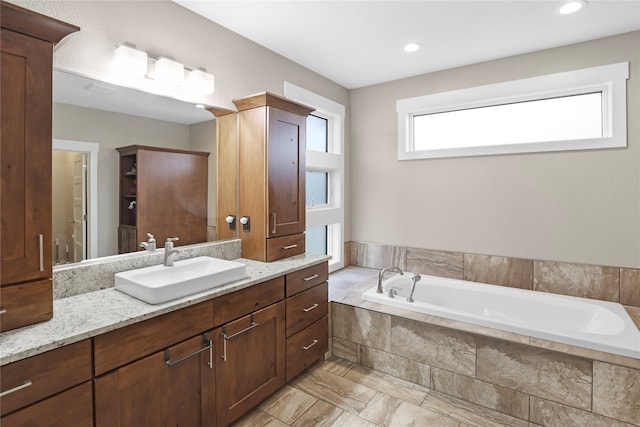 bathroom featuring a relaxing tiled tub and vanity