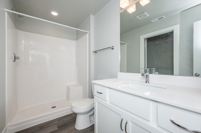 bathroom with hardwood / wood-style floors, vanity, toilet, and walk in shower