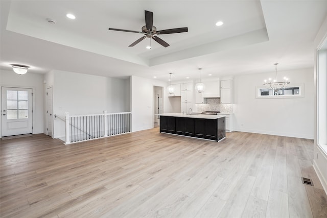 unfurnished living room featuring ceiling fan with notable chandelier, light hardwood / wood-style floors, a raised ceiling, and sink