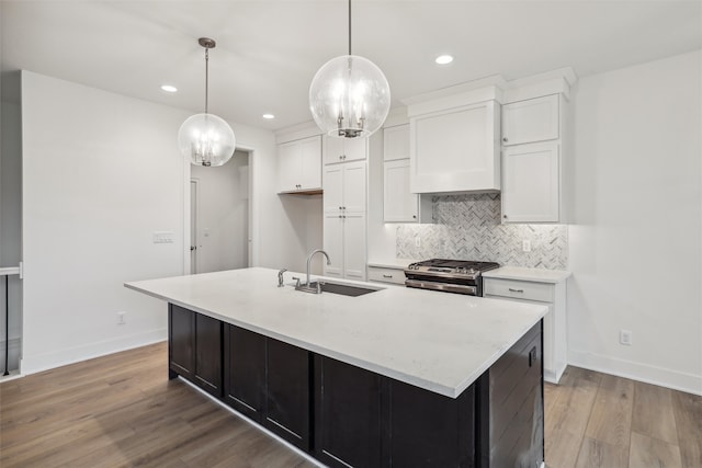 kitchen with white cabinets, a center island with sink, gas range, light wood-type flooring, and decorative light fixtures