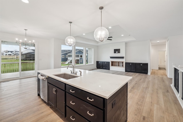 kitchen with light wood-type flooring, stainless steel dishwasher, sink, decorative light fixtures, and an island with sink