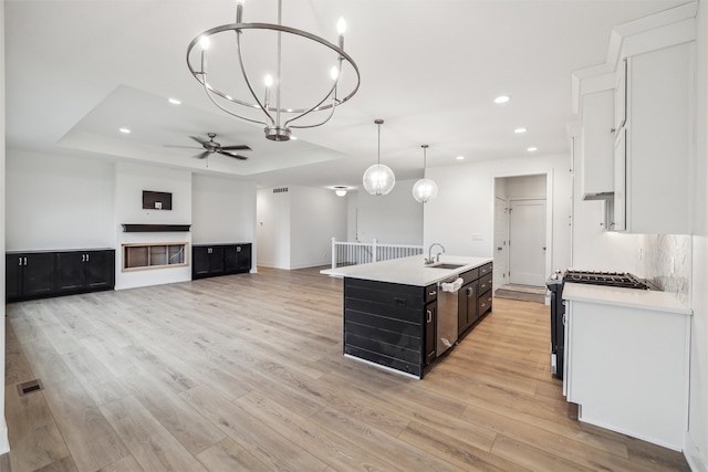 kitchen featuring hanging light fixtures, light wood-type flooring, a tray ceiling, and a kitchen island with sink