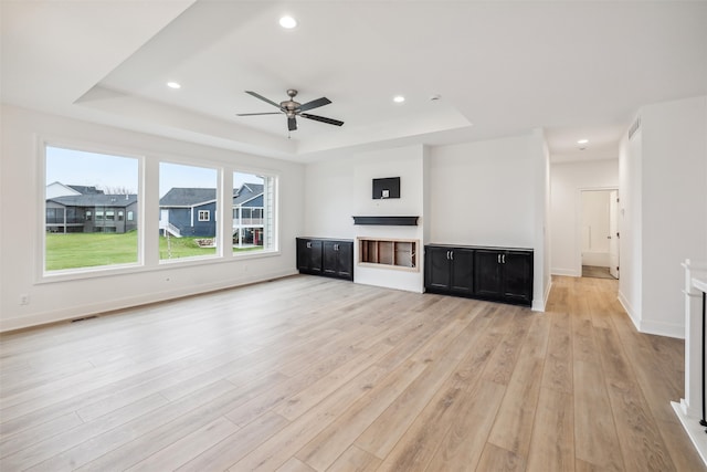 unfurnished living room with a tray ceiling, ceiling fan, and light hardwood / wood-style flooring