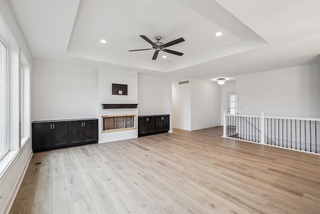 unfurnished living room with light hardwood / wood-style floors, a wealth of natural light, and a tray ceiling