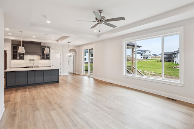 unfurnished living room with ceiling fan with notable chandelier, a raised ceiling, light wood-type flooring, and sink