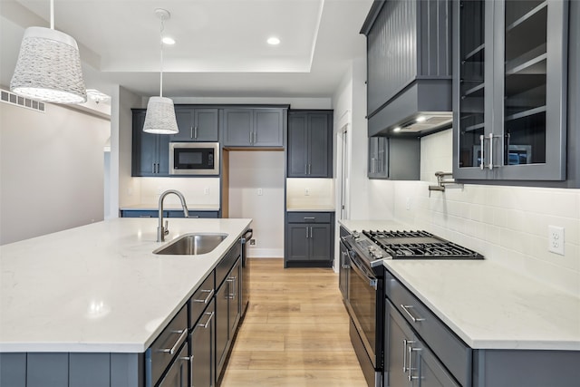 kitchen with sink, hanging light fixtures, appliances with stainless steel finishes, and light hardwood / wood-style flooring