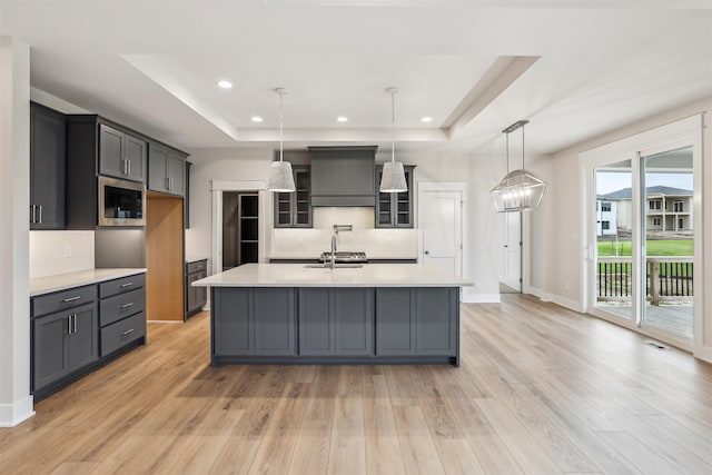 kitchen featuring stainless steel microwave, light hardwood / wood-style flooring, an island with sink, and pendant lighting