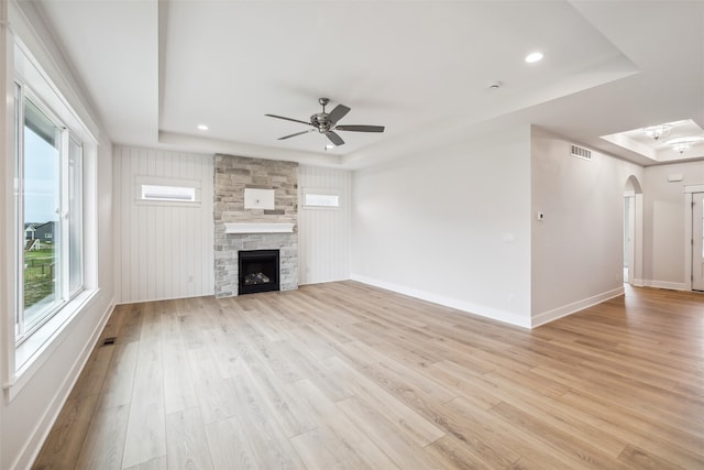 unfurnished living room featuring a tray ceiling, ceiling fan, a fireplace, and light wood-type flooring