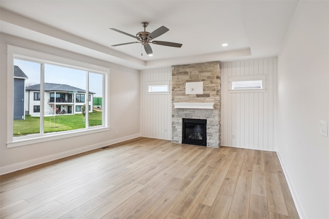 unfurnished living room with ceiling fan, a raised ceiling, light wood-type flooring, and a fireplace