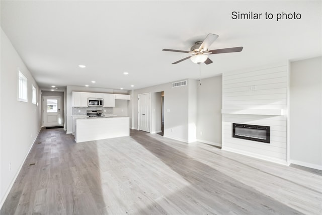 unfurnished living room with light wood-type flooring, a large fireplace, and ceiling fan